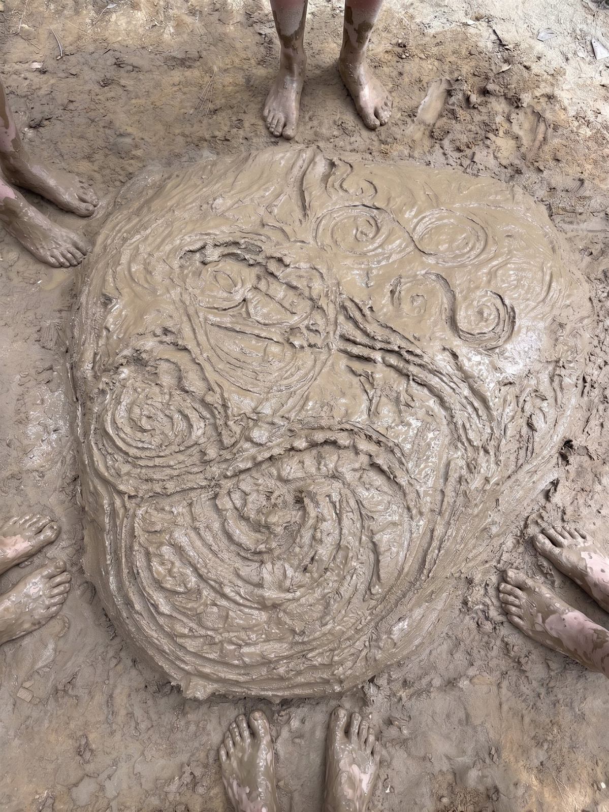 Bare feet around a batch of mud pugged into a spiral pattern