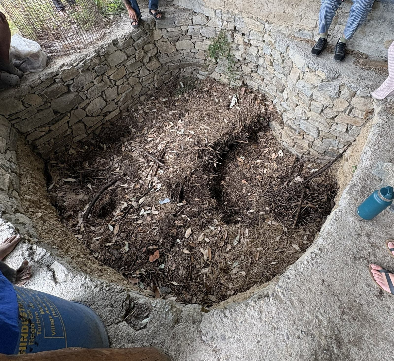 Stone-lined compost pit layered with leaf litter and garden waste